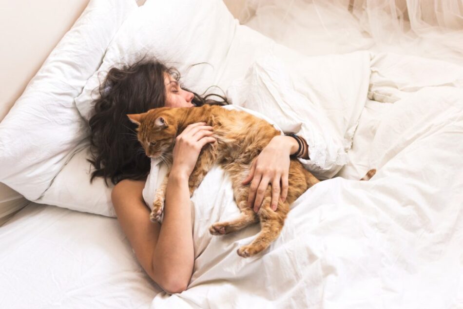 Una donna che dorme sul letto coccola il gatto