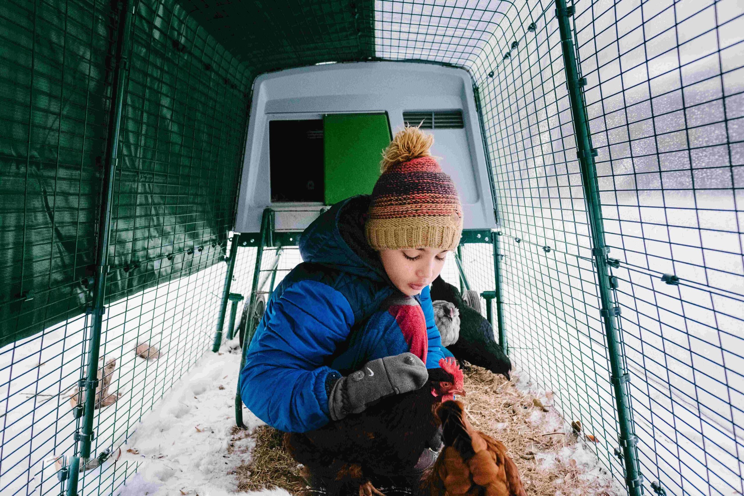 Un ragazzo accanto al pollaio Eglu con le galline e la neve