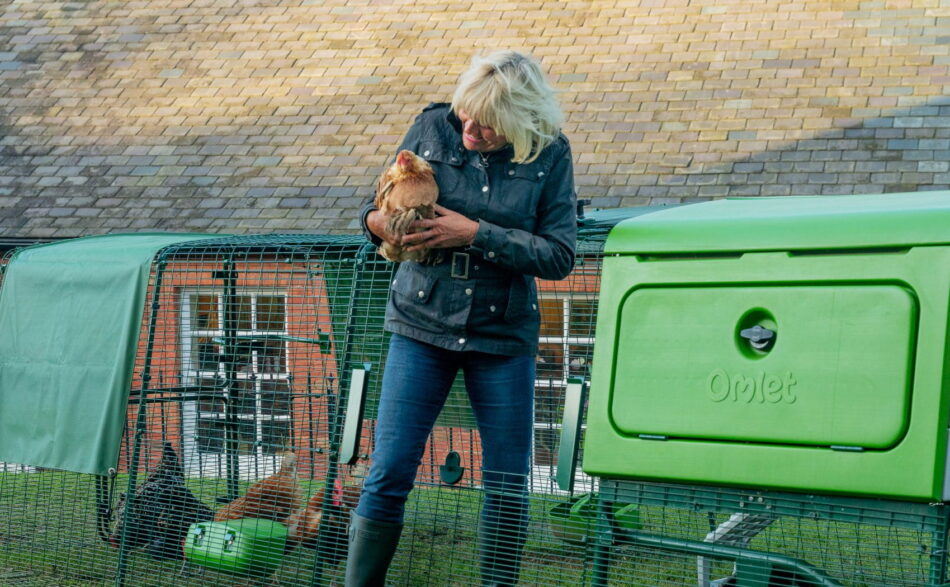 Donna con una gallina in braccio che esce dal recinto del pollaio Eglu Pro