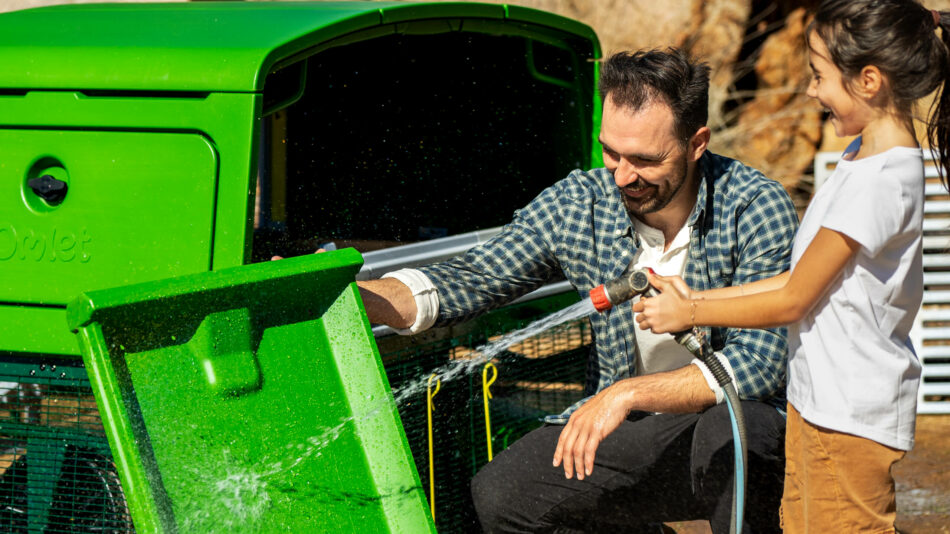 Uomo e bambina che puliscono il vassoio per le deiezioni di Eglu Pro di Omlet con un tubo da giardino
